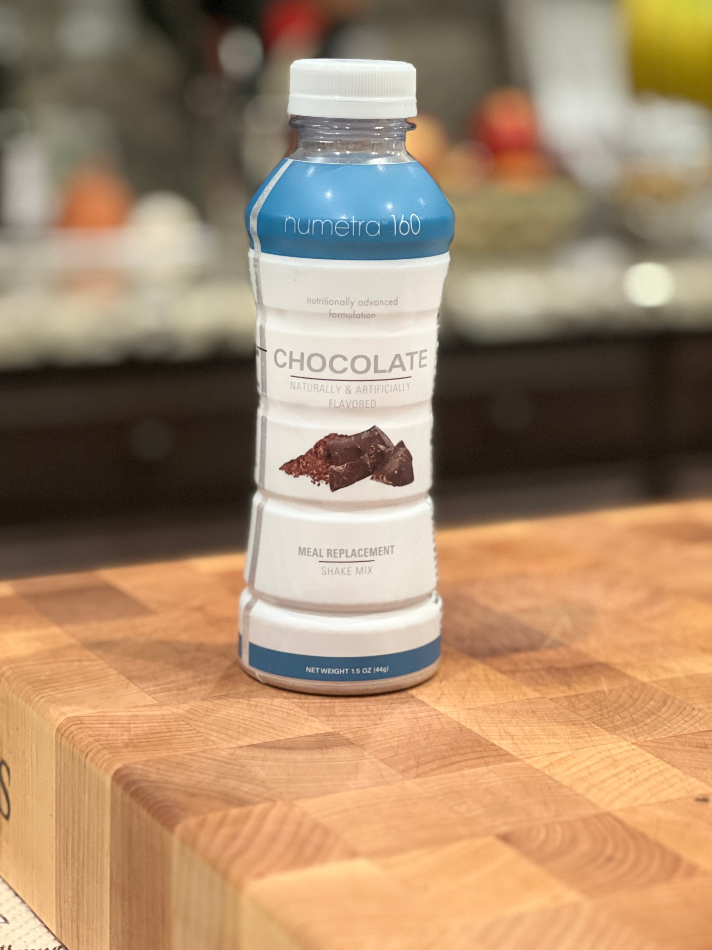 Product photography of a Numetra 160 chocolate meal replacement shake bottle on a butcher block counter.
