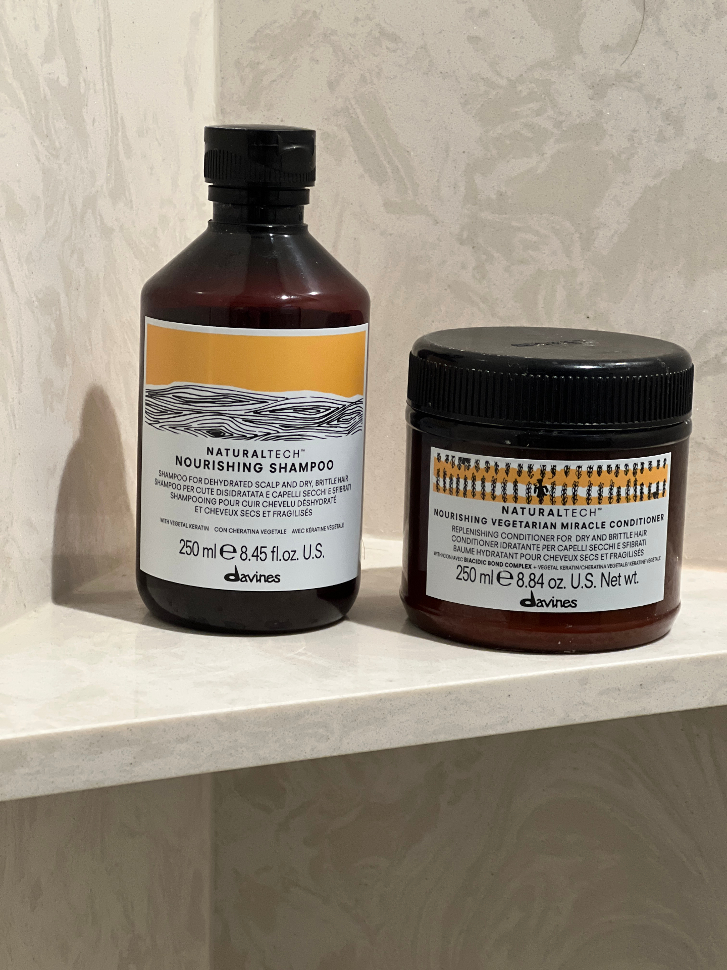 Product photography of Davines NaturalTech Nourishing Shampoo and Vegetarian Miracle Conditioner on a bathroom shelf.