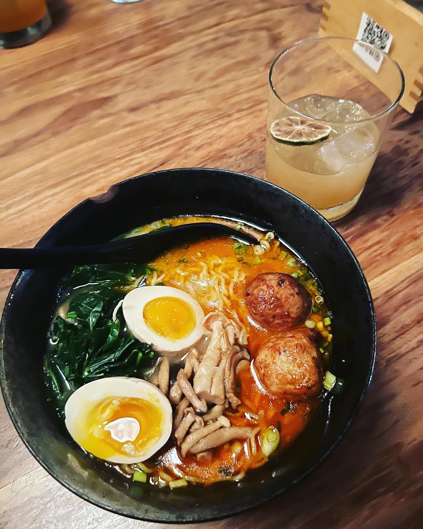 Product photography of a ramen bowl with soft egg, mushrooms, and meatballs alongside a citrus cocktail at Two Ten Jack in Nashville.